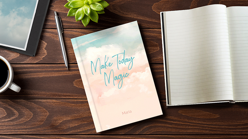 A personalized journal with a watercolor cloud cover and the text Make Today Magic, sitting on a desk.