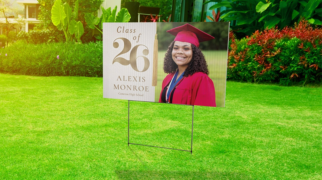 A Front Yard Celebration: A personalized graduation yard sign in a green lawn featuring a photo of a graduate in a red cap and gown with the text Class of 26 Alexis Monroe Cameron High School.