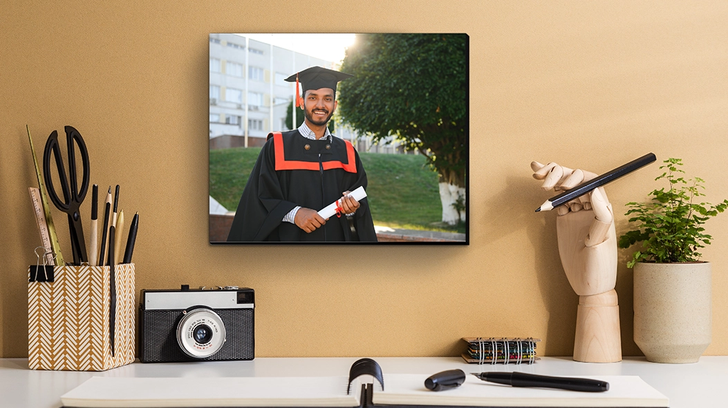 A Milestone Memory: A mounted photo print of a graduate in a black cap and gown holding a diploma, displayed on a wall above a desk with a camera and office supplies.