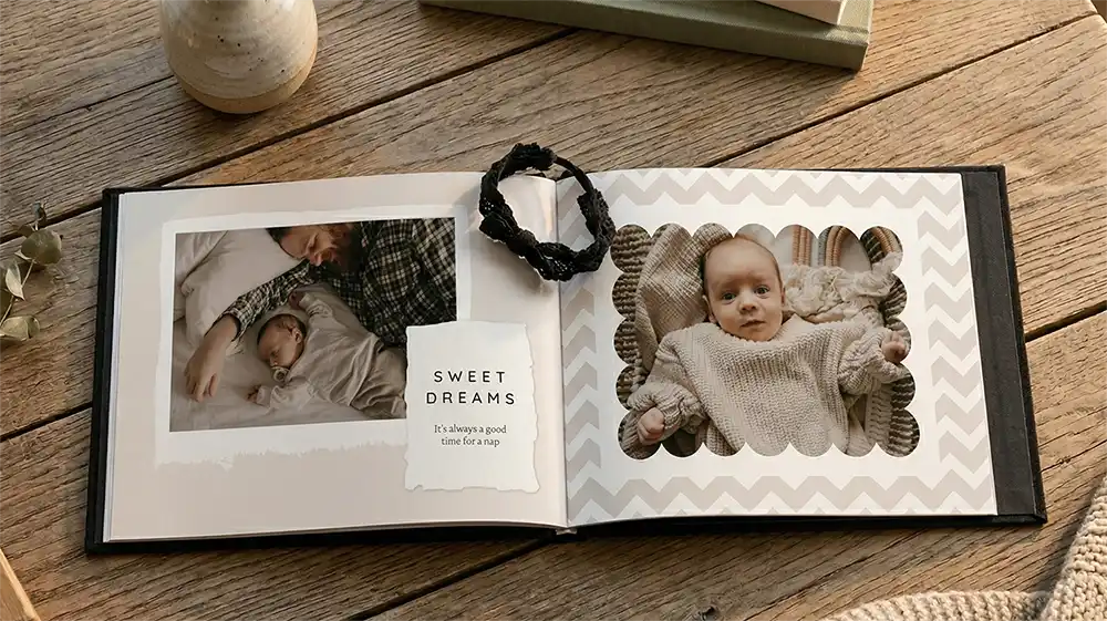 Same day photo books featuring an open black linen cover album with personalized baby photos on a wooden table.