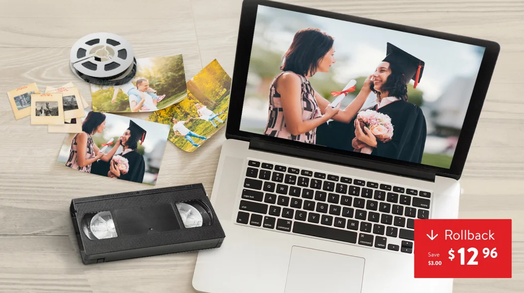 Home And Movie Transfer: A laptop displaying a graduation video next to a VHS tape, a film reel, and printed photographs on a light wooden surface.
