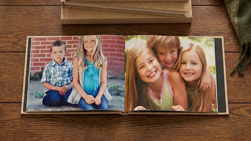 Same day photo books showcasing a tan linen album with high-resolution portraits of children on a natural wood background.