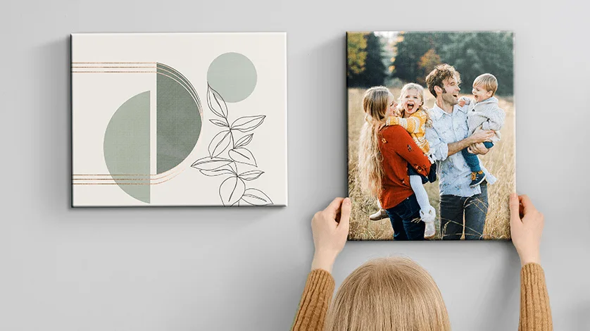 Same Day Wall Art: A person hangs a square canvas print of a family next to an abstract art canvas on a gray wall.